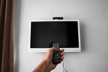 The man with the remote control in hand want switch on the TV and presses the button on the remote control. Remote control in hand closeup.