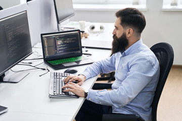 Computer programmer developer working in IT office, sitting at desk and coding, working on a...