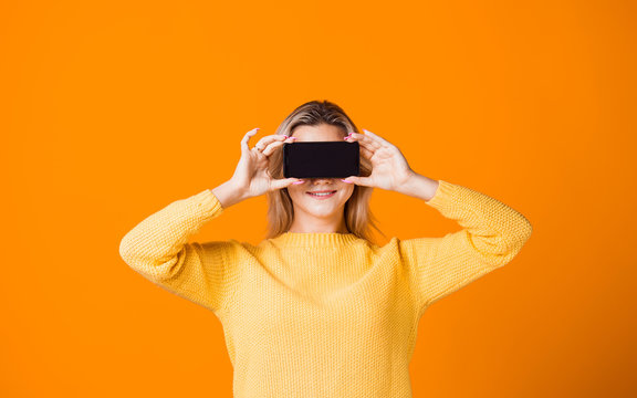 Cute young woman in a yellow sweater holding a smartphone