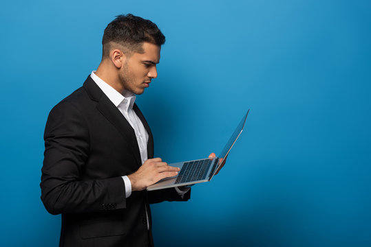 Side View Of Businessman Using Laptop On Blue Background