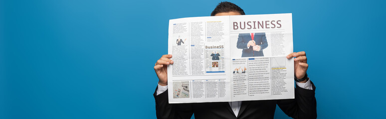 Fototapeta na wymiar Panoramic shot of businessman covering face while reading newspaper isolated on blue