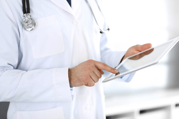 Doctor man using tablet computer for network research or virtual disease treatment, hands close-up. Perfect medical service in clinic. Modern medicine, medic data and healthcare concepts. Toned