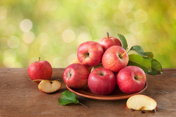 Ripe red-yellow apples with leaves in a clay plate on a wooden table. Whole and sliced fruits. Harvest fruit trees.