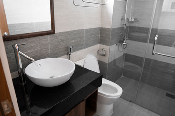 Bathroom interior with white round sink and chrome faucet in a modern bathroom with a toilet and shower. Water flowing from the chrome faucet.