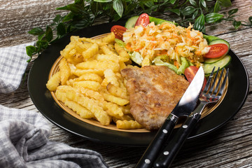 Fried pork chop in breadcrumbs, served with fries and salad.