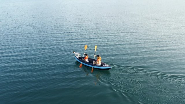 Aerial view happy mother, son, dog drone rowing on inflatable kayak on water large lake background picturesque cliffs and green vegetation, beautiful sunset day. Family sports. Lifestyle. Lens flare