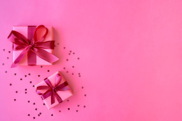 Two gift boxes with ribbon and bow on pink background with heart shaped confetti. Top view and space for text