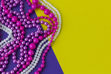 Mardi Gras or Fat Tuesday composition. Multi colored mardi gras beads on yellow and purple paper background. Flat lay, copy space for text.