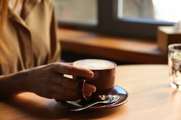Woman with aromatic coffee at table in cafe, closeup