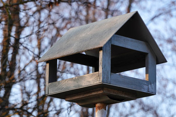 wooden bird feeder in the Park, made in the form of a house, in the background autumn forest and trees. feeding birds in winter