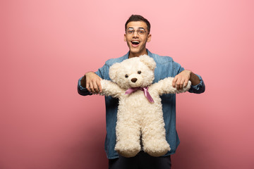 Surprised man with teddy bear looking at camera on pink background