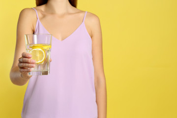 Young woman with glass of lemon water on yellow background, closeup. Space for text