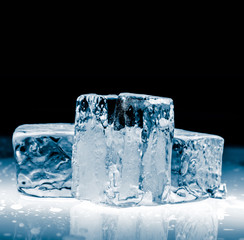 Crystal clear transparent blue shiny ice blocks, on reflective surface on black background.