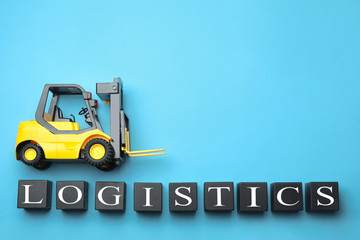 Flat lay composition with toy forklift and word LOGISTICS on light blue background, space for text. Wholesale concept
