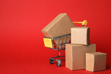 Shopping cart and boxes on red background, space for text. Logistics and wholesale concept © New Africa