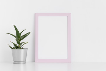 Pink frame mockup with a aloe vera in a pot on a white table. Portrait orientation.