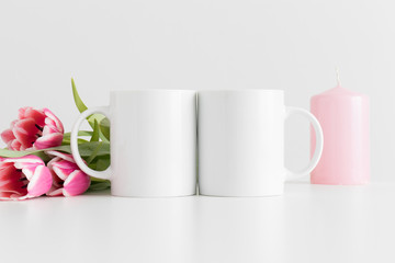 Two mugs mockup with pink tulips and a candle on a white table.