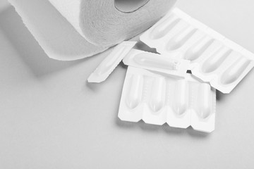 Suppositories and toilet paper on light background. Hemorrhoid treatment