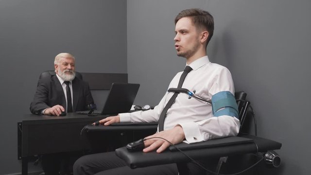 Senior expert checking handsome man with computer polygraph