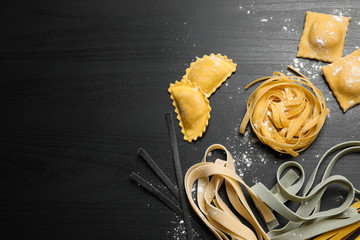 Flat lay composition with different types of pasta on black wooden table