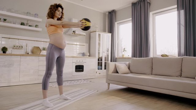 pregnant woman doing squats with ball at home