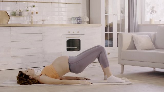 side view of pregnant woman exercising at home on fitness mat