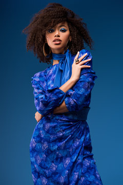 attractive african american woman in dress looking at camera isolated on blue