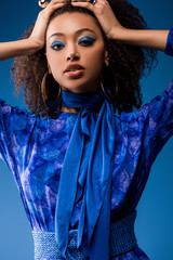 attractive african american woman in stylish dress looking at camera isolated on blue