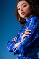 low angle view of attractive african american woman in stylish dress looking at camera isolated on blue