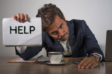 depressed and stressed attractive hispanic man in suit and tie working overwhelmed office computer desk holding notepad asking for help frustrated and overworked