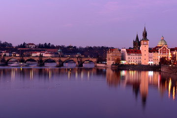 Urban scene with old Town Bridge Tower, clock tower and St. Francis Of Assisi Church in Prague, Czech Republic while sunset