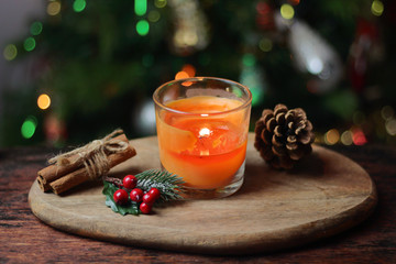 Beautiful Christmas orange mandarin candle on a wooden stand with sticks of whole cinnamon, sprig of mistletoe and a Christmas tree decorated with toys. Christmas New year evening mood, greeting card