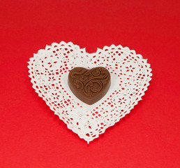 Chocolate heart is centered on a white paper lace heart-shaped doily on a red background.