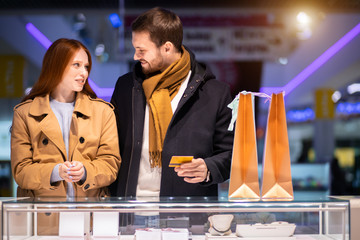 beautiful lovely cute couple in shopping mall together, decided to buy jewelry for woman, man holding discount card in hands going to buy ring