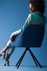 african american woman sitting on armchair on blue background