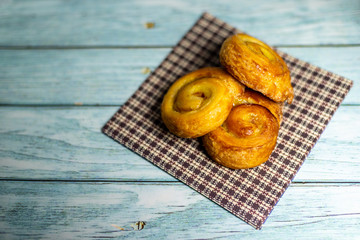 Homemade glazed puff pastry cinnamon rolls on a napkin against a dark blue wooden background. ...