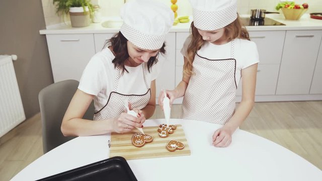 Charming mother and cute daughter glazing ginger cookies