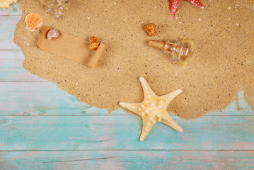 Starfish with seashells on sea sand on wooden background. Papyrus from the glass bottle with cork.