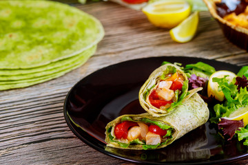 Spinach wrap with meat and vegetables on black plate with green salad.