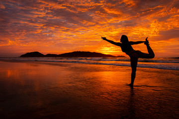 Silhouette of young woman doing Yoga dancer pose on sunrise at Campeche beach in Florianopolis Brazil