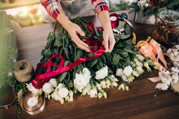 Fototapeta na wymiar top view on florist female tying bouquet of wonderful flowers with red ribbon, florist in her own flowers shop enjoy work with plants, preparing them for sale