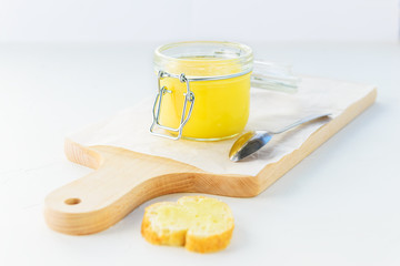 Ghee butter in a jar with a slice of loaf on a white table.