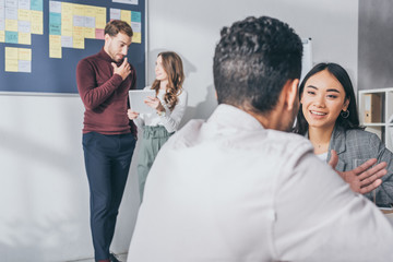 selective focus of asian businesswoman looking at man near coworkers