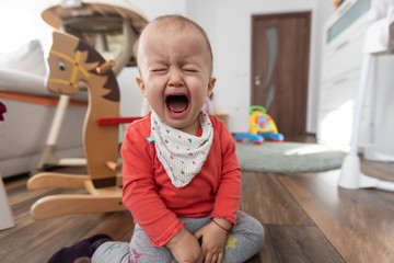Little girl sitting on the floor at home and crying. One year old baby crying