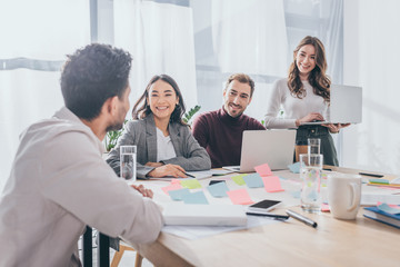 selective focus of happy multicultural coworkers looking at businessman in office
