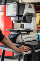 Arbeiterhand an Digitalem Messprojektor mit Komputer und Messtisch, Glasmessfläche,...