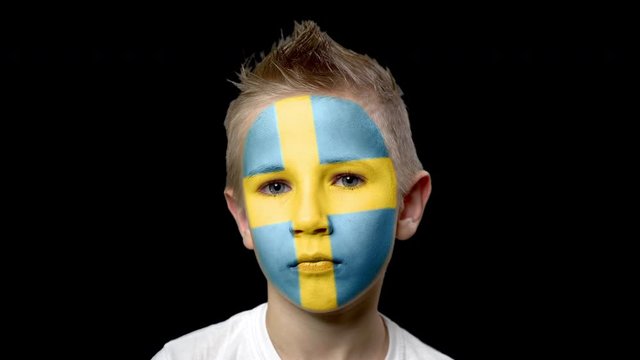 Sad fan of the football team of Sweden. A child with a face painted in national colors. Unhappy boy with sad eyes. Fiasco of your favorite team. Disappointment. Sadness. Experience. Failure. Bad luck.