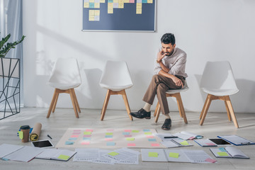 Fototapeta premium pensive mixed race businessman sitting on chair near sticky notes