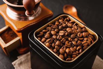 Coffee beans in a black metal jar, cotton cloth, vintage coffee grinder, wooden brown spoon on a dark concrete background