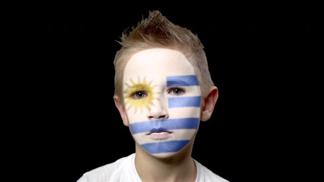 Sad fan of the football team of Uruguay. A child with a face painted in national colors. Unhappy boy with sad eyes. Fiasco of your favorite team. Disappointment. Sadness. Experience. Failure. Bad luck